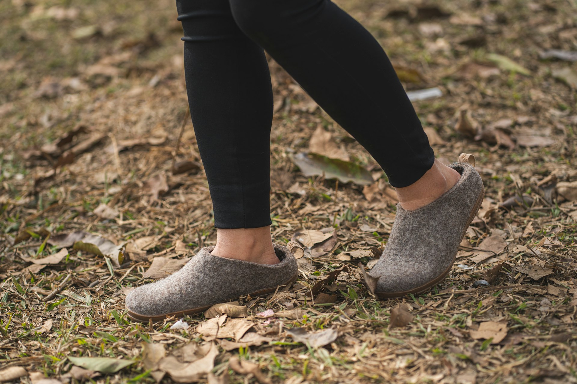 Legs in black leggings walking over autumn leaves in grey felt slipper-clogs